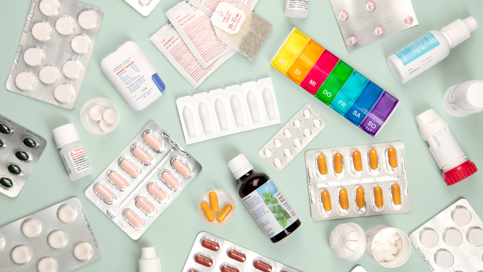 Vielfalt moderner Medikamente Verschiedene Medikamente wie Tabletten, Kapseln, Fläschchen und ein farbiger Wochendosierer auf hellgrünem Hintergrund.