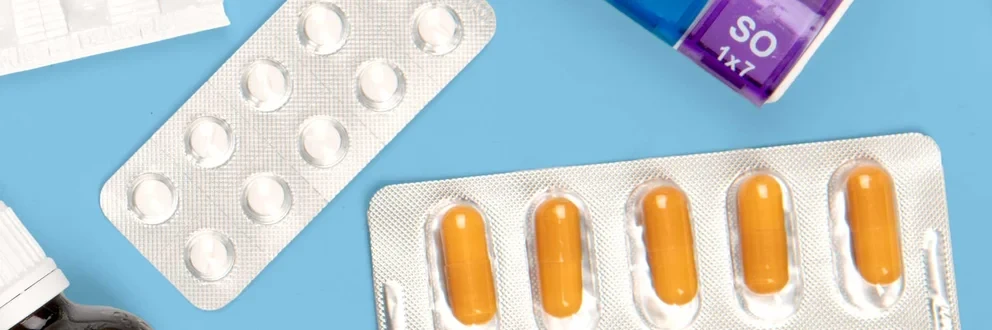 Vielfalt moderner Medikamente Verschiedene Medikamente wie Tabletten, Kapseln, Fläschchen und ein farbiger Wochendosierer auf hellblauem Hintergrund.