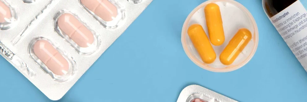 Vielfalt moderner Medikamente Verschiedene Medikamente wie Tabletten, Kapseln, Fläschchen und ein farbiger Wochendosierer auf hellblauem Hintergrund.