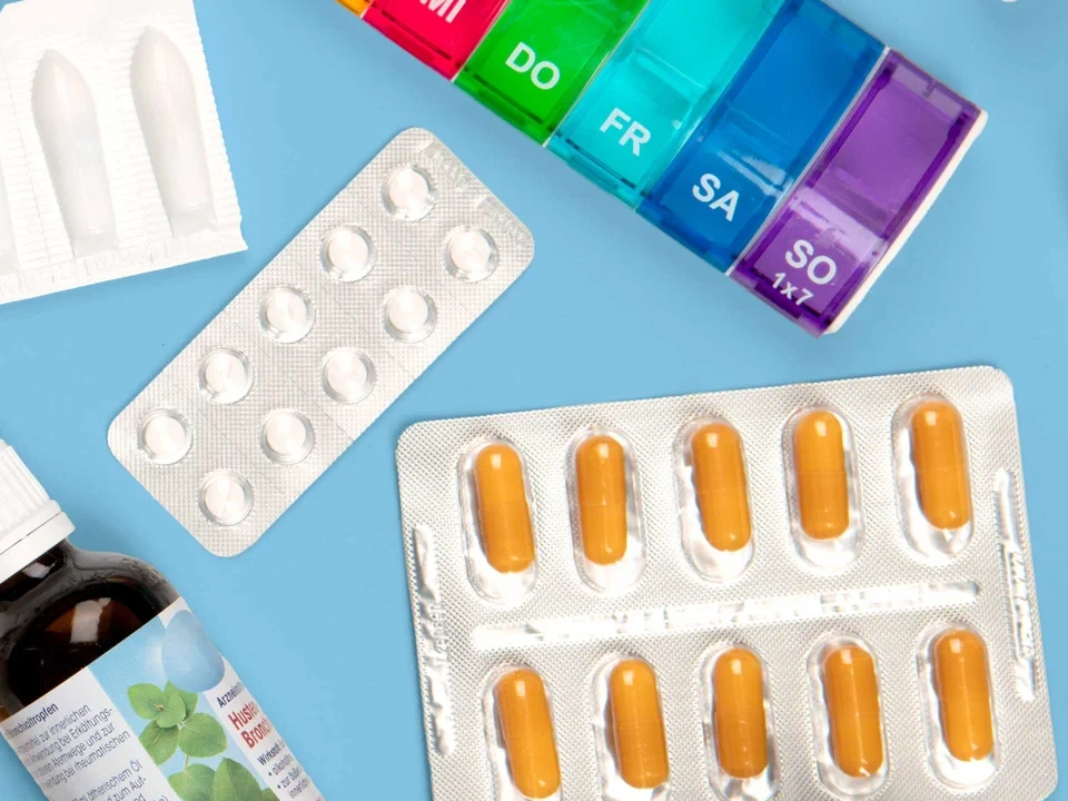 Vielfalt moderner Medikamente Verschiedene Medikamente wie Tabletten, Kapseln, Fläschchen und ein farbiger Wochendosierer auf hellblauem Hintergrund.