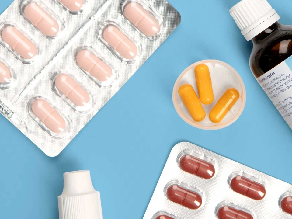 Vielfalt moderner Medikamente Verschiedene Medikamente wie Tabletten, Kapseln, Fläschchen und ein farbiger Wochendosierer auf hellblauem Hintergrund.