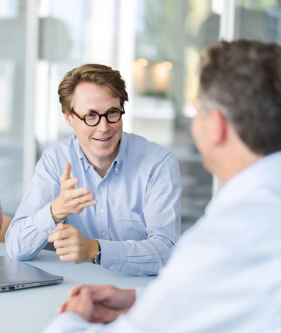 Drei Personen diskutieren an einem Tisch mit Laptops in einem hellen, modernen Büro. Drei Personen diskutieren an einem Tisch mit Laptops in einem hellen, modernen Büro.