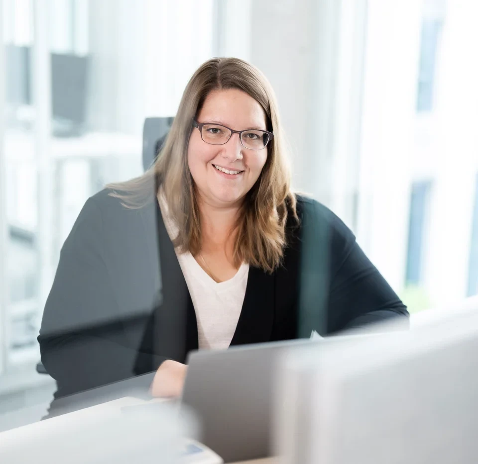 Eine Person mit langen Haaren sitzt an einem Schreibtisch und arbeitet an einem Computer. 